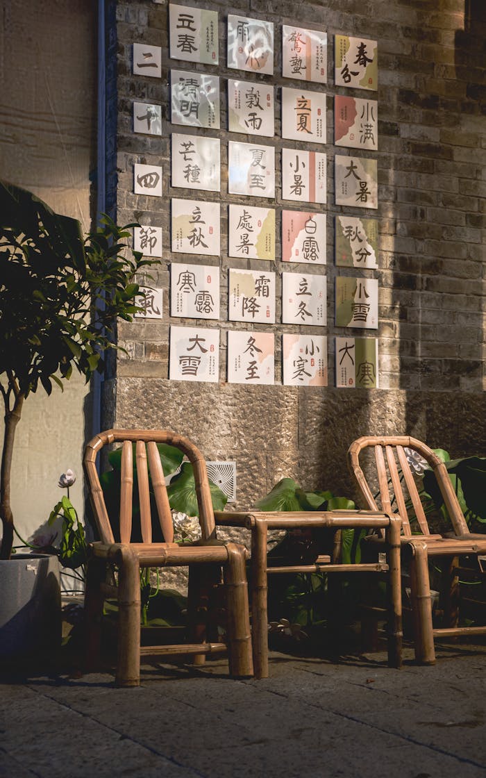 Services-02 Bamboo chairs in front of a brick wall adorned with Chinese calligraphy cards in a serene outdoor setting.