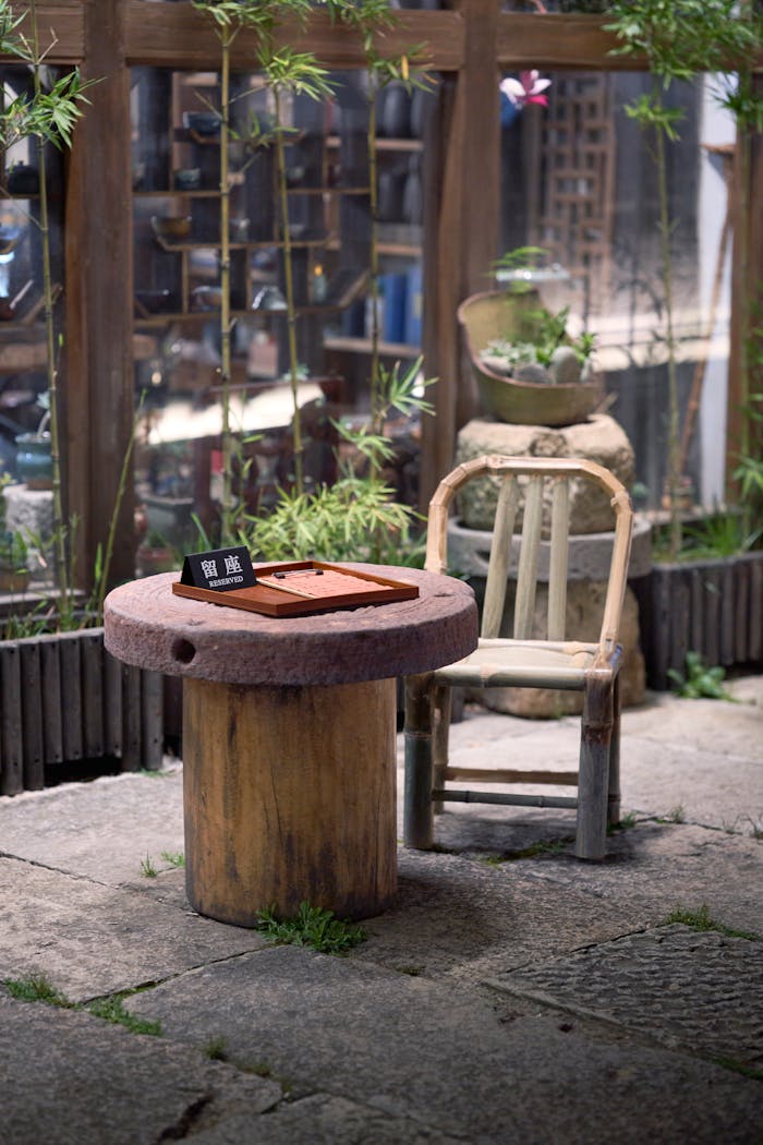 Services-03 Charming rustic scene with a bamboo chair and round stone table outdoors.