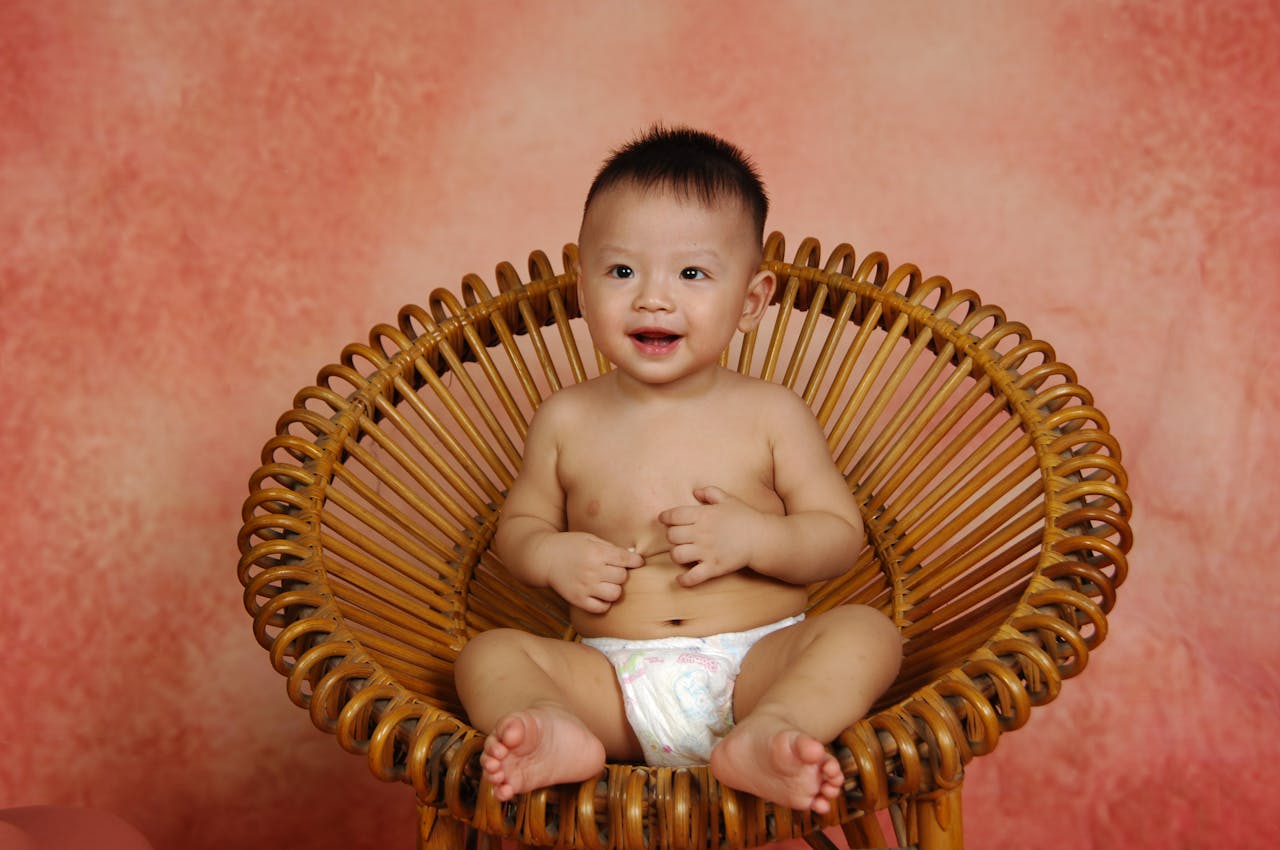digital Charming baby in a diaper sitting on a circular bamboo chair, smiling.